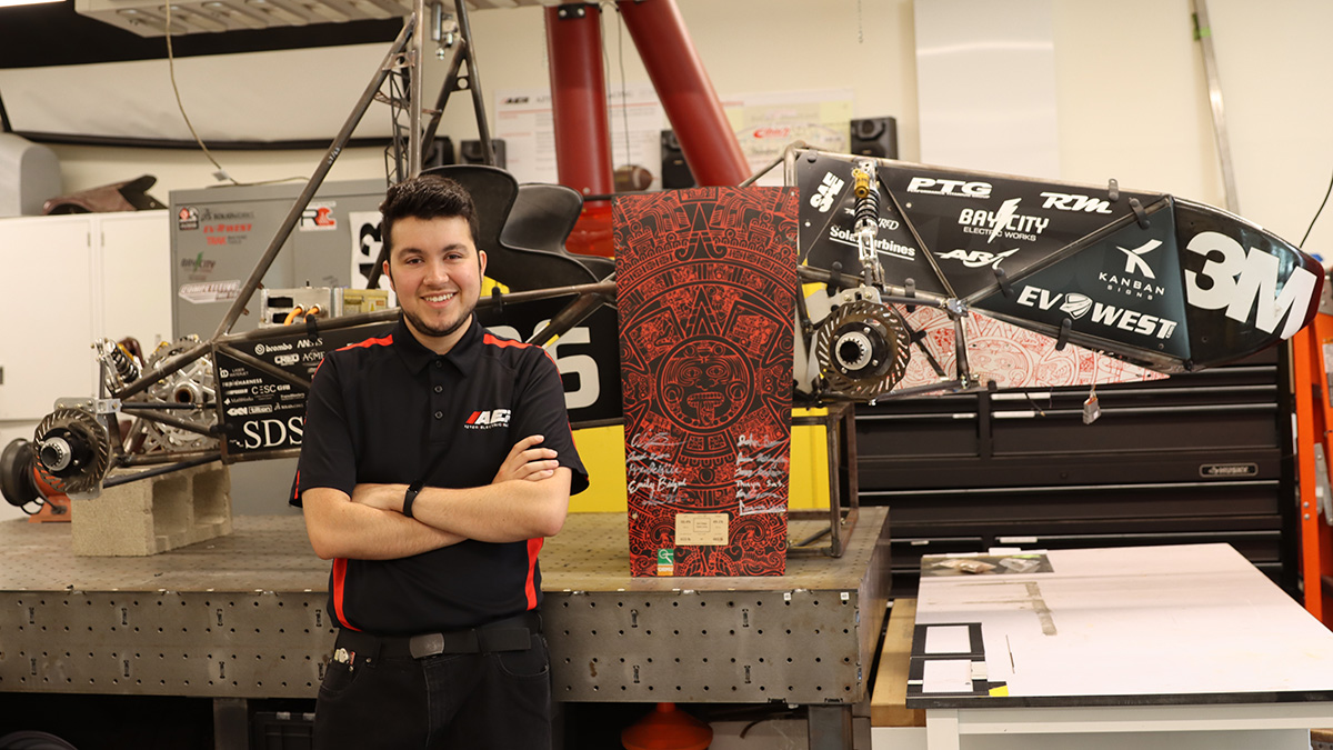 Student poses in front of electric racing car